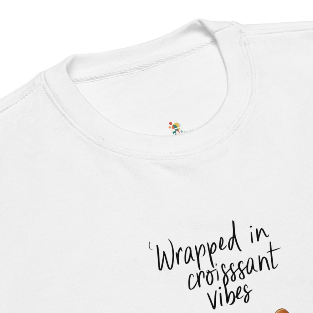 White t-shirt with 'Wrapped in croissant vibes' text and colorful design on a white background