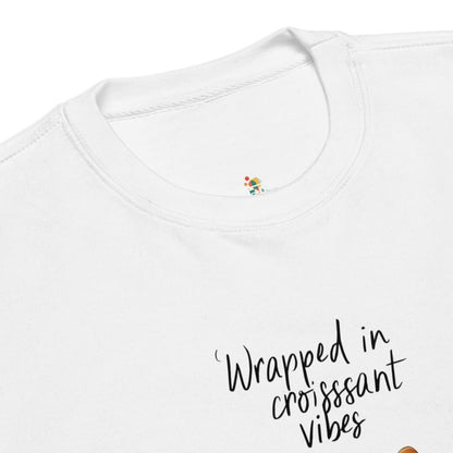 White t-shirt with 'Wrapped in croissant vibes' text and colorful design on a white background