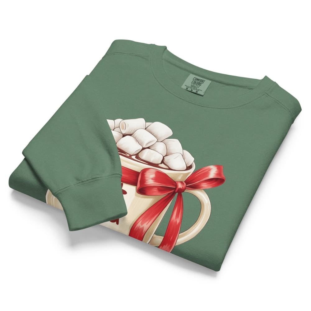 Folded green sweatshirt with a hot chocolate graphic featuring marshmallows and a red bow on a white background.