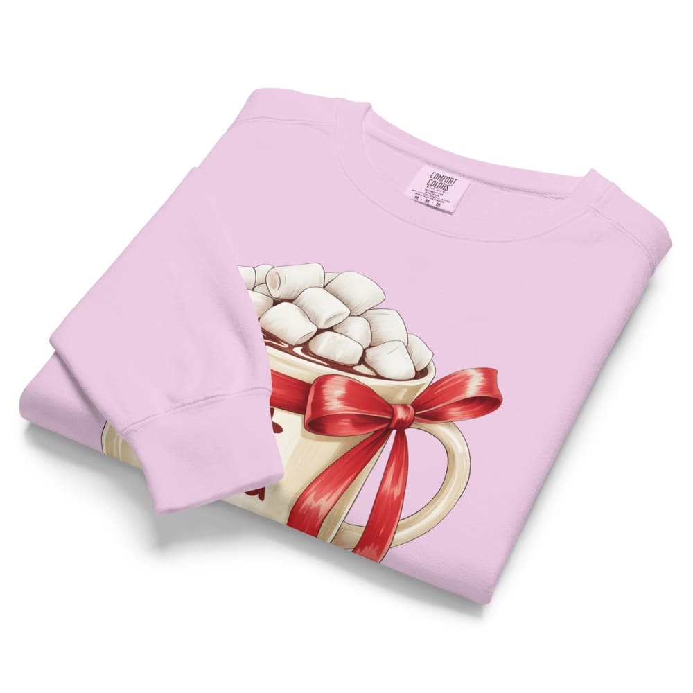 Folded pink sweatshirt with a graphic of a mug of hot chocolate with marshmallows and a red bow on a white background.