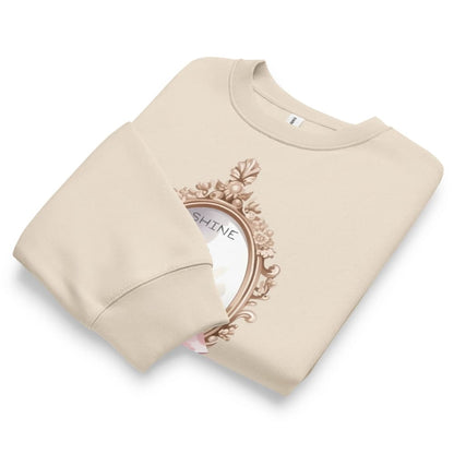 Beige sweatshirt with decorative emblem and 'SHINE' text on a white background