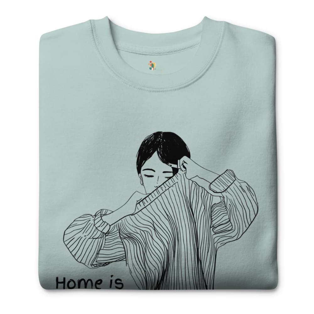 Folded light blue sweatshirt with a black and white illustration of a person wearing a sweater and 'Home is' text.