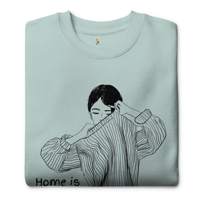 Folded light blue sweatshirt with a black and white illustration of a person wearing a sweater and 'Home is' text.