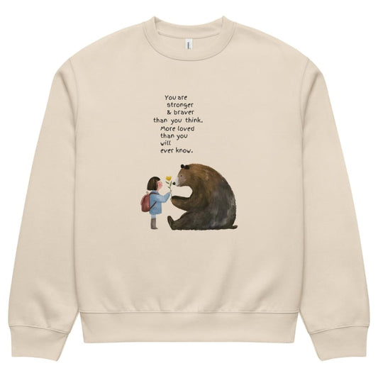 Beige sweatshirt with a graphic of a girl and bear holding hands and text on a white background