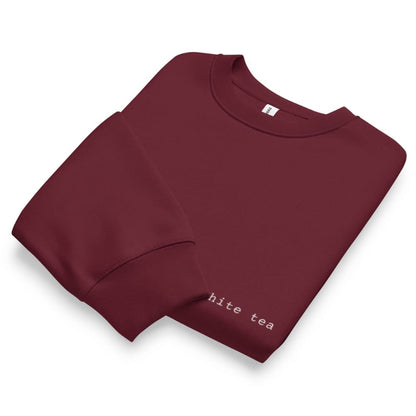 Folded maroon sweatshirt with 'hite tea' text on a white background