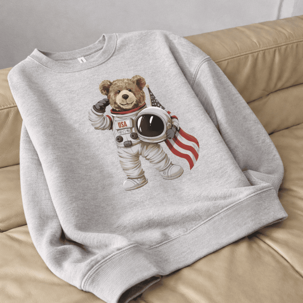 Gray sweatshirt with a teddy bear astronaut design on a beige couch.