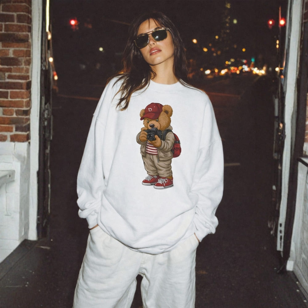 Person wearing a white sweatshirt with a teddy bear graphic on a city street at night.