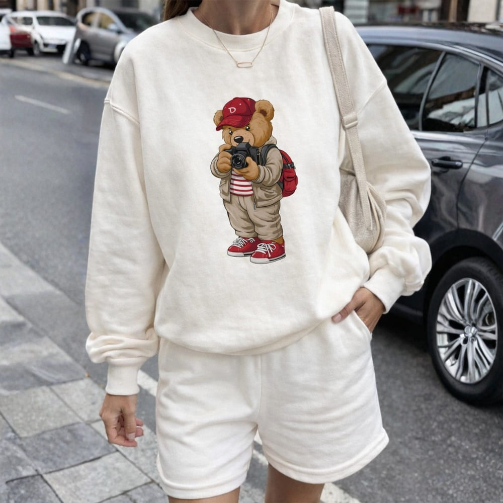 Person wearing a white sweatshirt with a teddy bear graphic on a city street.