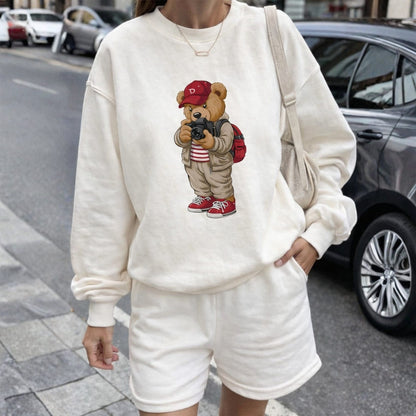 Person wearing a white sweatshirt with a teddy bear graphic on a city street.