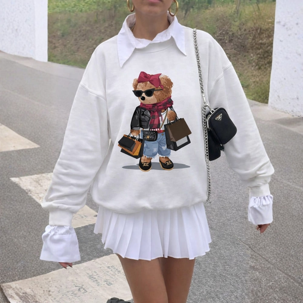 Person wearing a white sweatshirt with a teddy bear graphic, white pleated skirt, and black handbag.