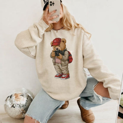 Person wearing a beige hoodie with a teddy bear graphic, taking a mirror selfie.