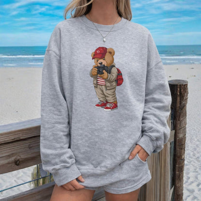 Person wearing a gray sweatshirt with a teddy bear graphic on a beach.