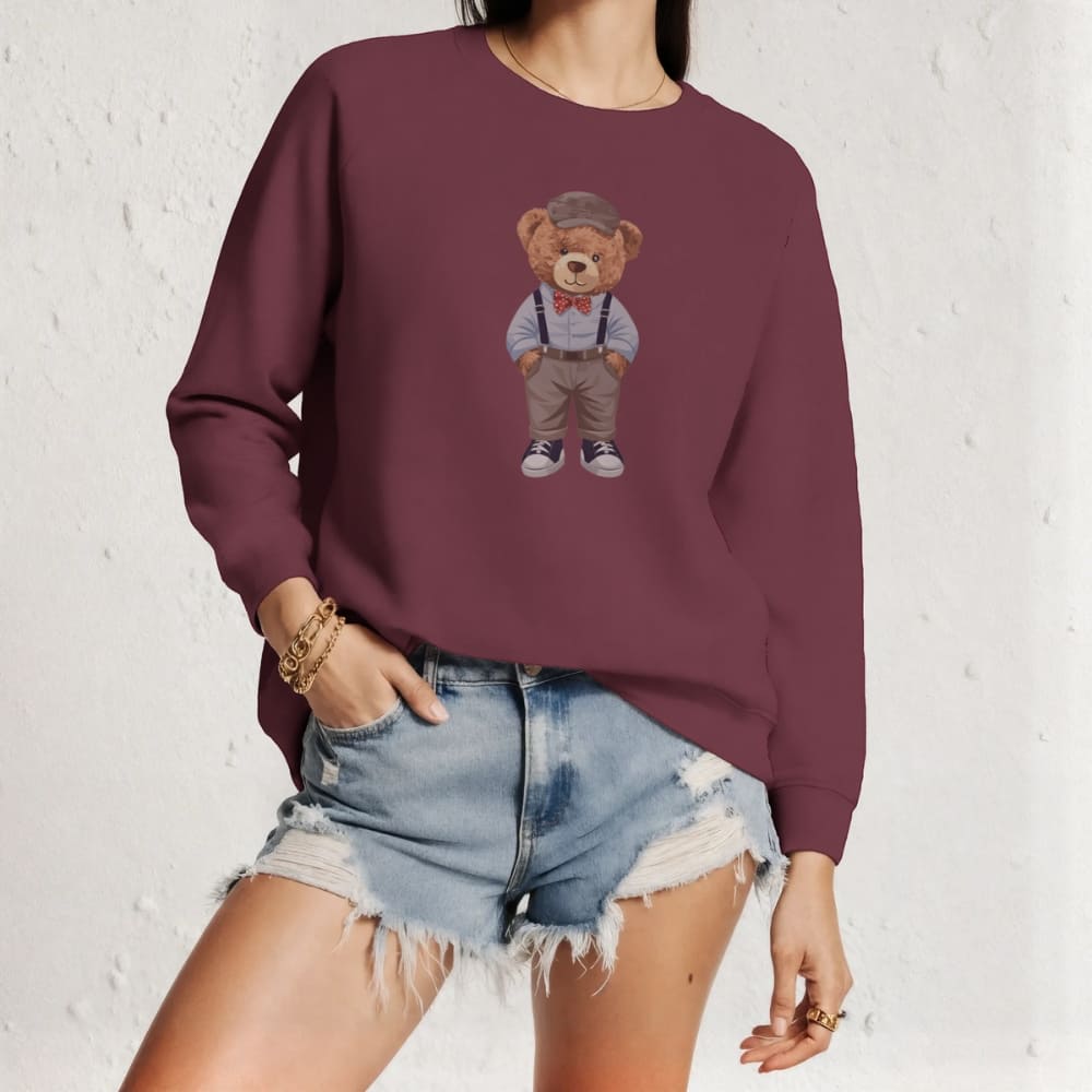 Person wearing a maroon sweatshirt with a teddy bear design against a white brick wall.