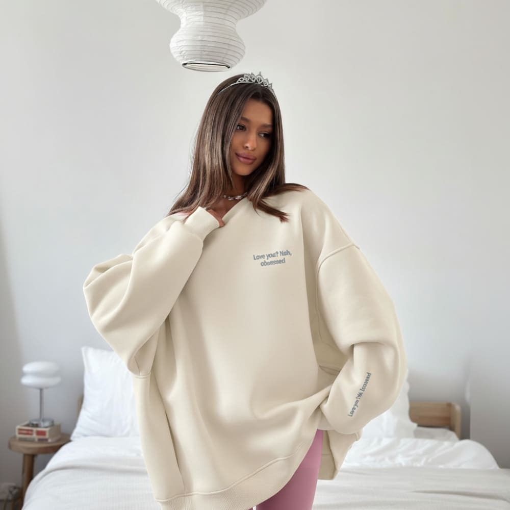 Woman wearing a beige oversized sweatshirt with text in a bedroom setting