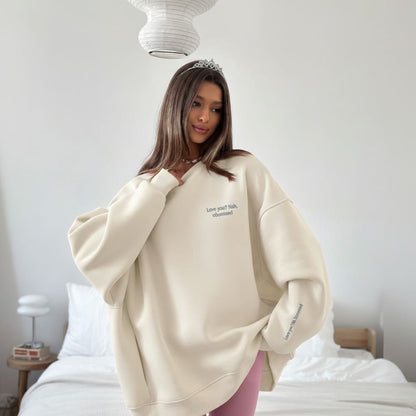 Woman wearing a beige oversized sweatshirt with text in a bedroom setting