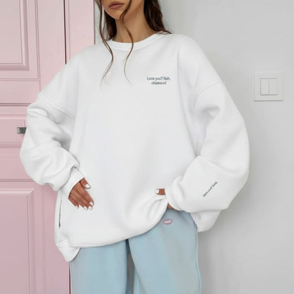 Person wearing a white oversized sweatshirt with text in front of a pink door.