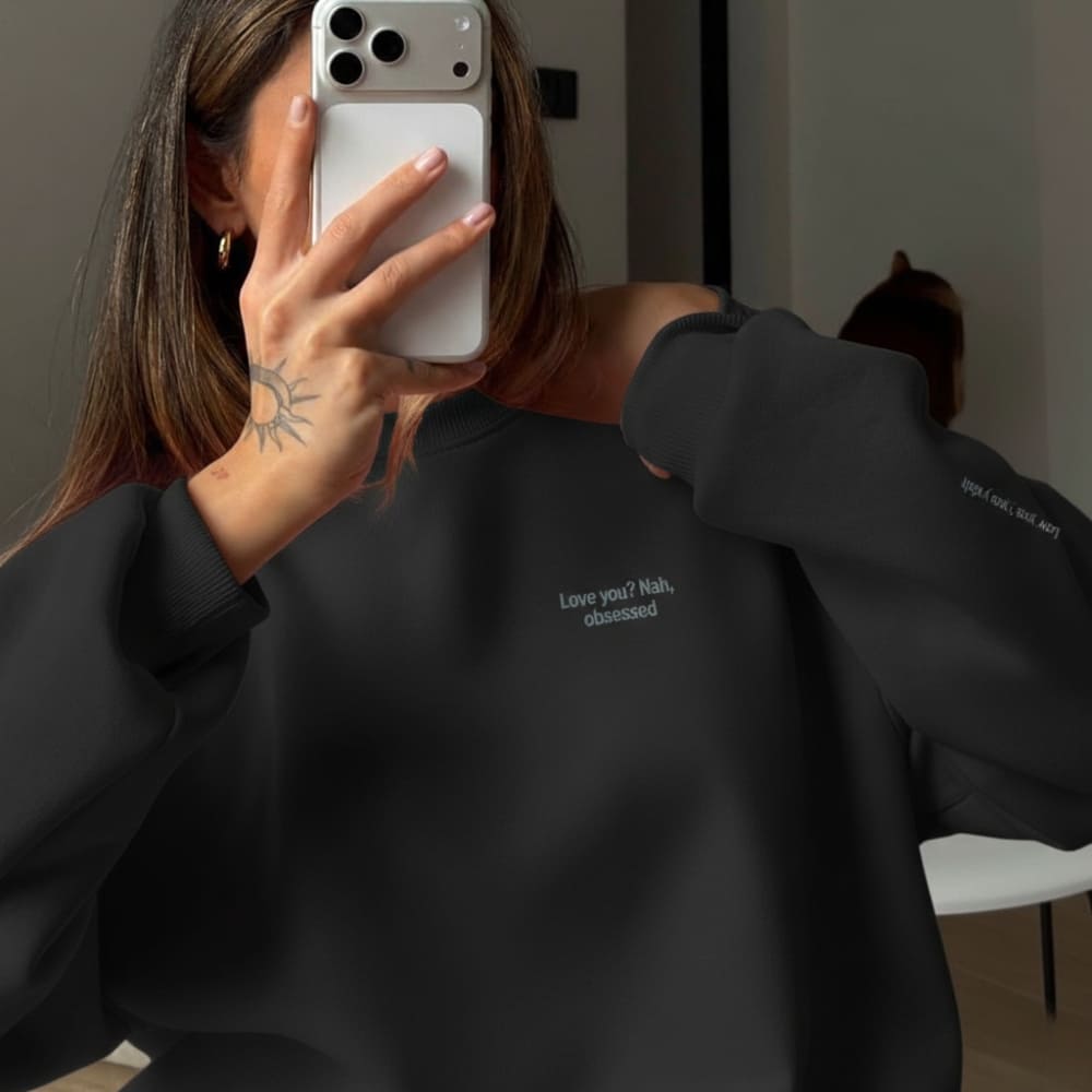Person wearing a black sweatshirt with text, holding a phone.