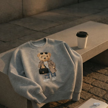 Gray sweatshirt with a teddy bear design on a stone bench with a coffee cup.