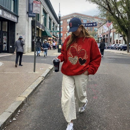 Person wearing a red sweatshirt with heart designs on a city street.