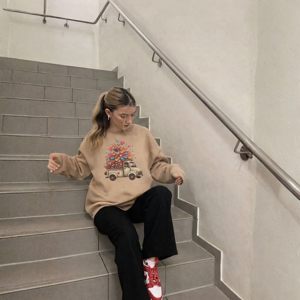 Woman sitting on a staircase wearing a beige sweater with a graphic design, black pants, and red shoes.