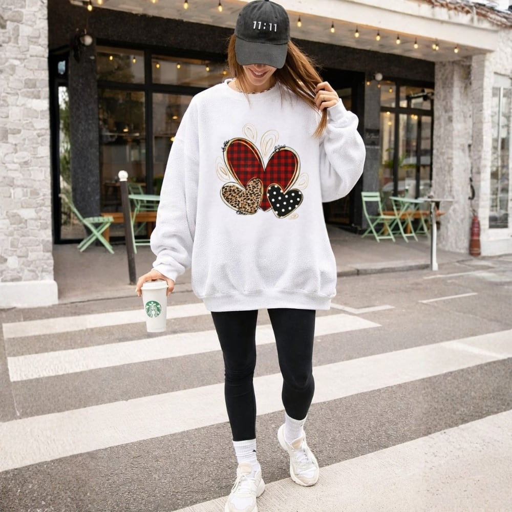 Person wearing a white sweatshirt with colorful designs, black leggings, and white sneakers, holding a Starbucks cup on a street.