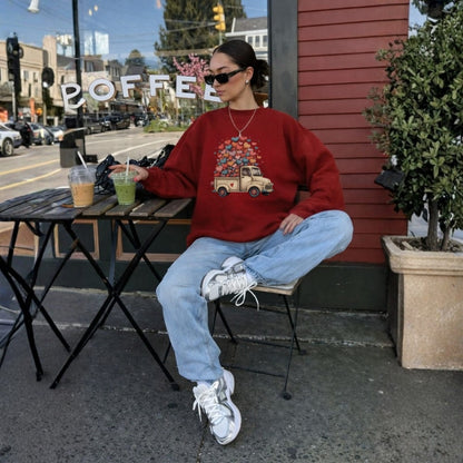 Person sitting outdoors at a coffee shop, wearing a red sweatshirt with a graphic design.