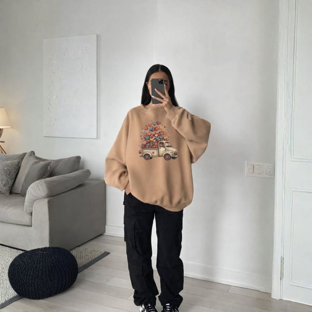 Person wearing a beige sweatshirt with a graphic design in a room with a gray sofa and lamp.