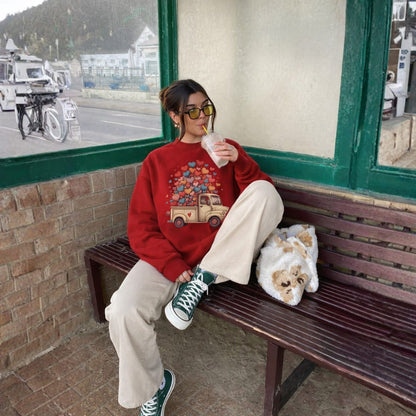 Person sitting on a bench wearing a red sweater with a car design, holding a drink, and wearing sunglasses.