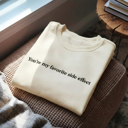 Folded beige sweatshirt with text on a textured surface near a window