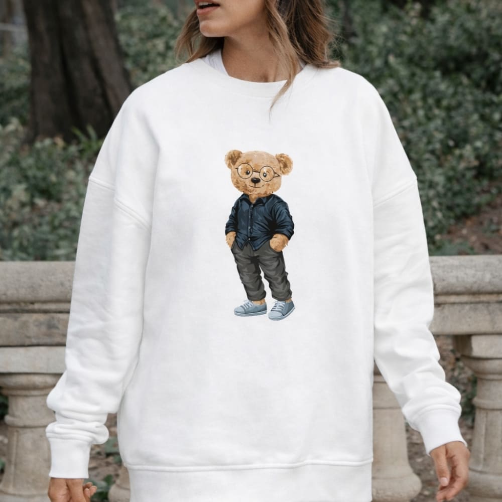 White sweatshirt with a teddy bear design worn by a person outdoors.