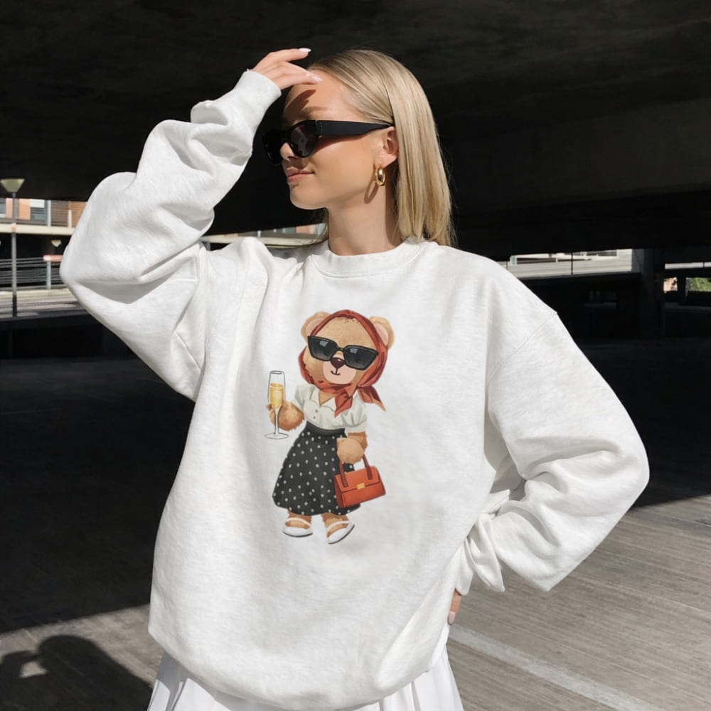 Woman wearing a white sweatshirt with a teddy bear graphic, standing in an urban setting.