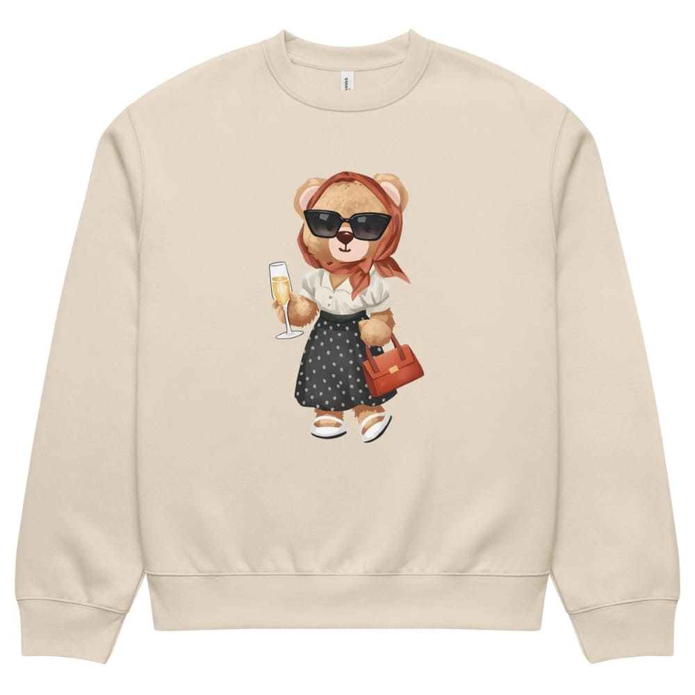 Beige sweatshirt with a teddy bear design holding a glass of champagne and a handbag on a white background