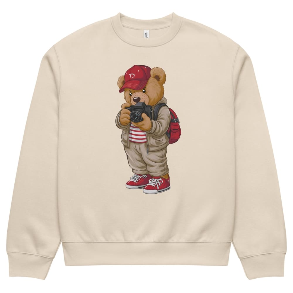 Beige sweatshirt with a cartoon bear wearing a red cap and backpack holding a camera on a white background