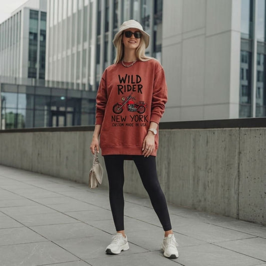 Woman wearing a red sweatshirt with 'Wild Rider New York' text, standing in an urban setting.
