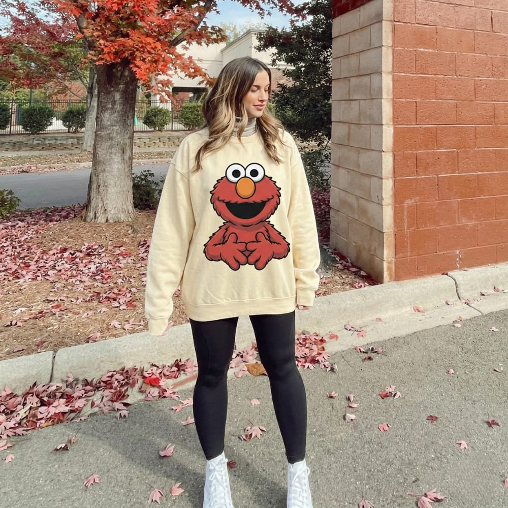 Person wearing a beige sweatshirt with a red character design outdoors.