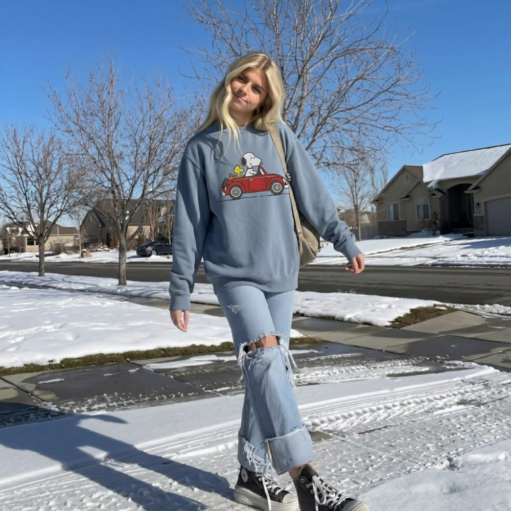 Person wearing a blue sweatshirt with a graphic design, walking on a snow-covered street.