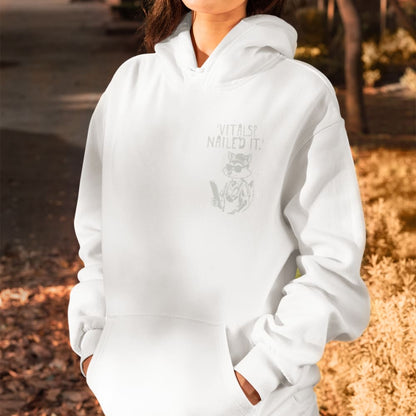 Raccoon nurse graphic wearing scrubs and sunglasses holding a clipboard under the quote “Vitals? Nailed It.” – printed on a black Cotton Heritage hoodie