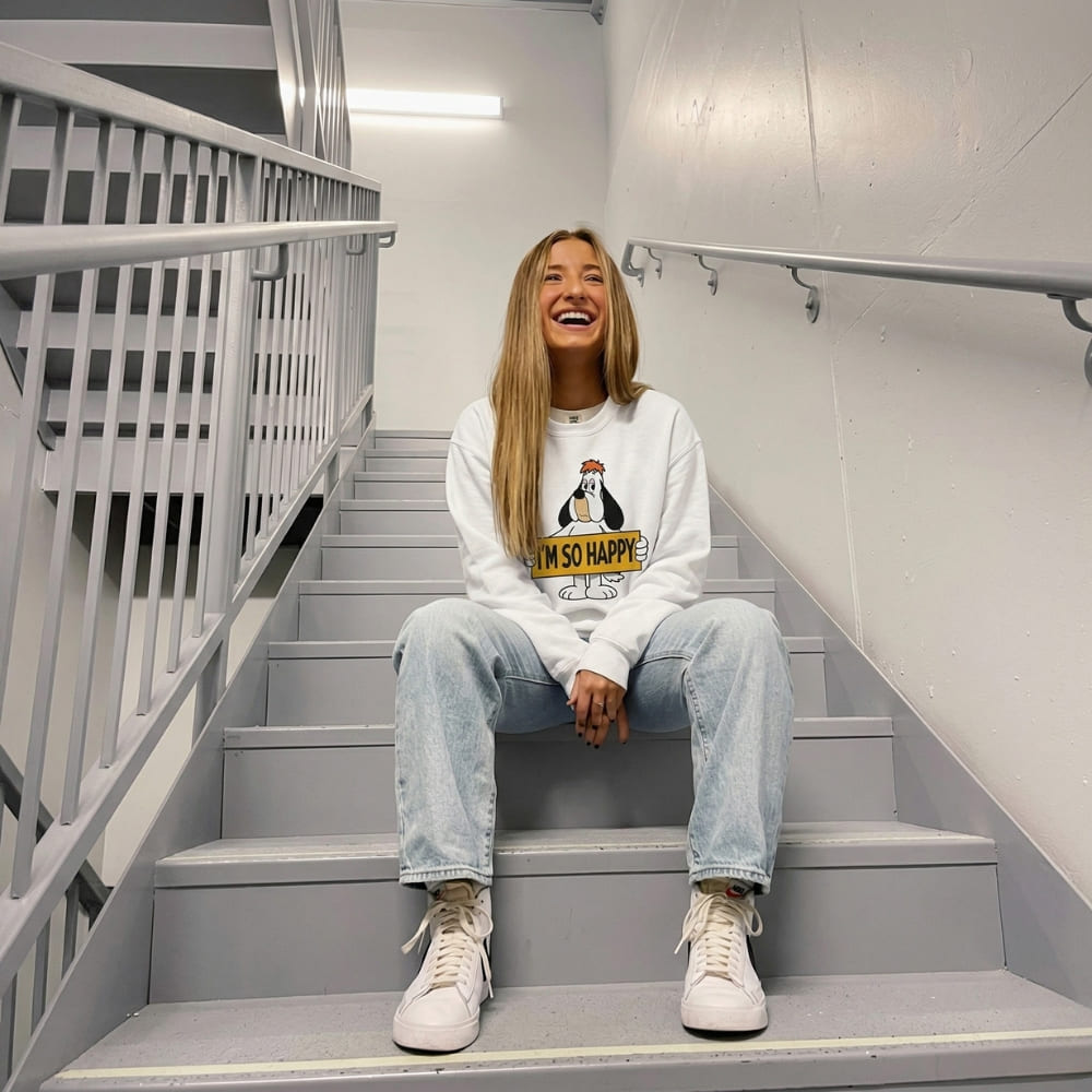 Person sitting on a staircase wearing a white sweatshirt with a graphic design and text.