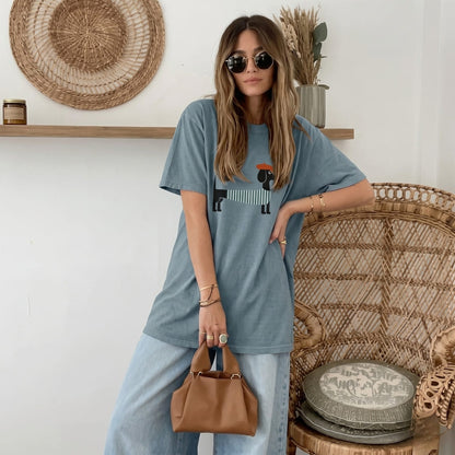 Woman wearing a blue t-shirt and jeans, holding a brown handbag, in a room with wicker furniture.