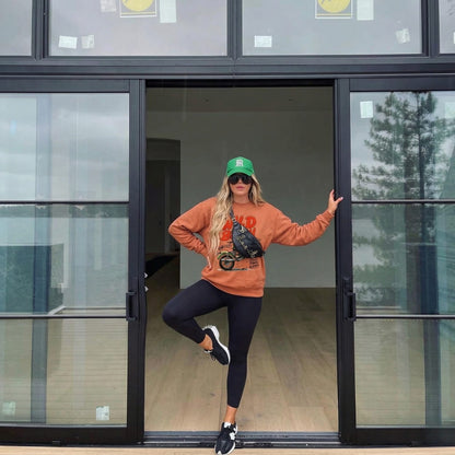 Person posing in front of a glass door wearing an orange sweatshirt and black leggings.