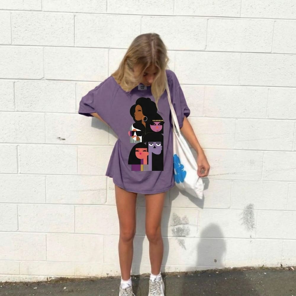 Person wearing a purple oversized t-shirt with graphic design against a white brick wall.