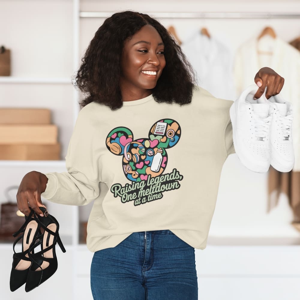 Woman wearing a sweatshirt with a colorful design and text, holding shoes and a bag.