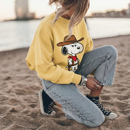 Person wearing a yellow sweatshirt with a cartoon character sitting on the beach.