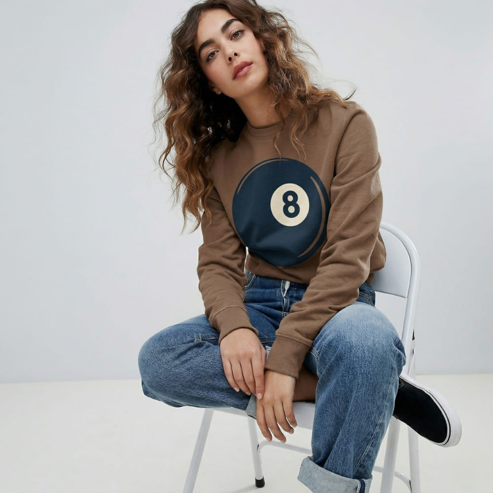 Woman wearing a brown sweatshirt with a circular design sitting on a white chair.