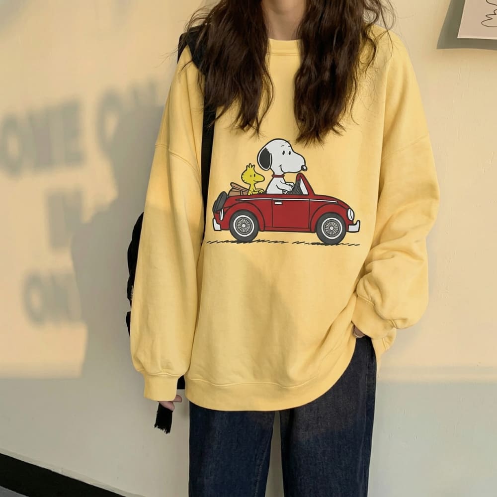 Person wearing a yellow sweatshirt with a cartoon design of Snoopy and Woodstock in a car.