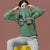 Person wearing a green sweatshirt with text and graphics on a brown background