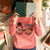 Person wearing a pink sweatshirt with text, holding a book over their face in a desk setting.