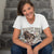 Woman wearing a white t-shirt with a graphic design and text, sitting on steps.