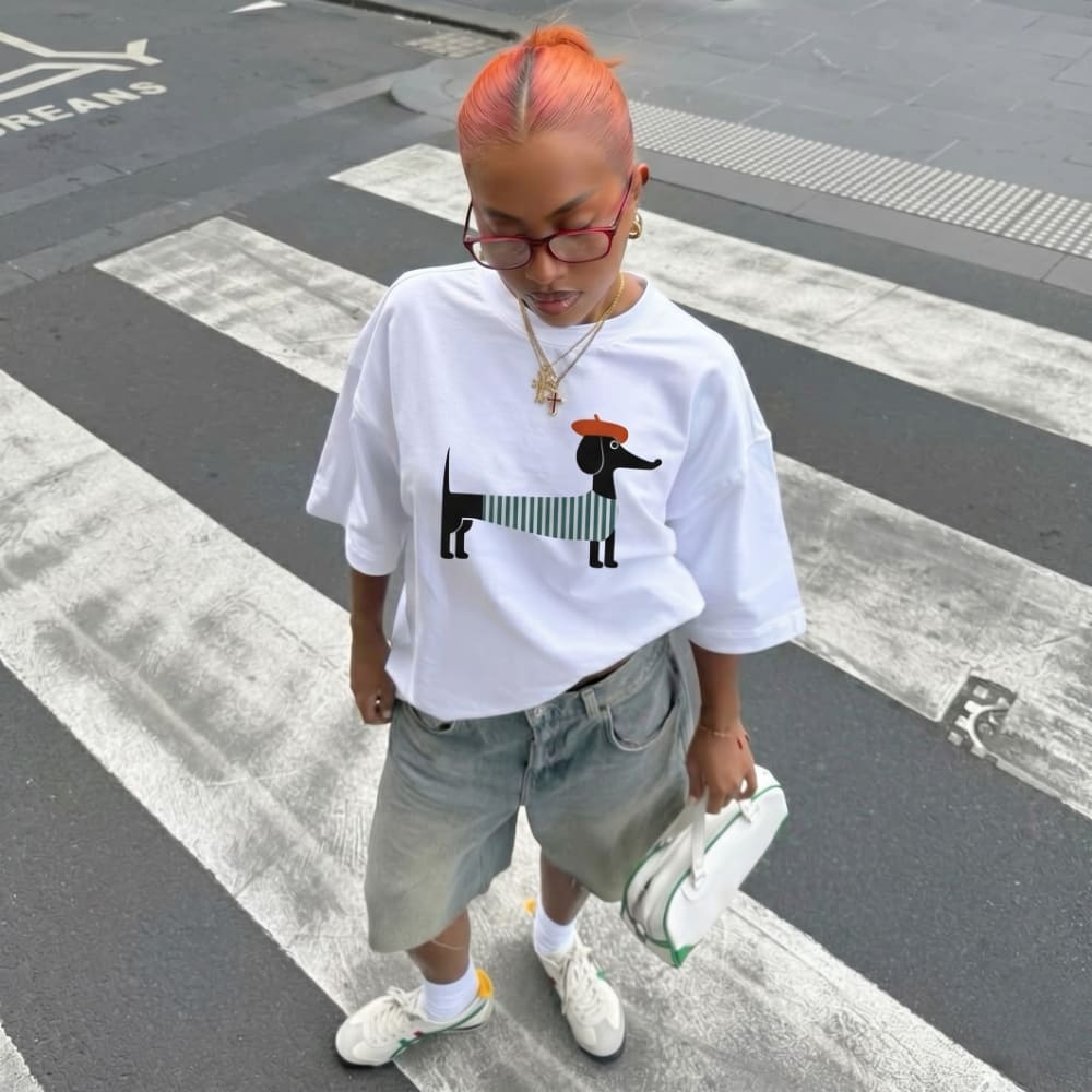 Person wearing a white t-shirt with a graphic design, standing on a crosswalk.