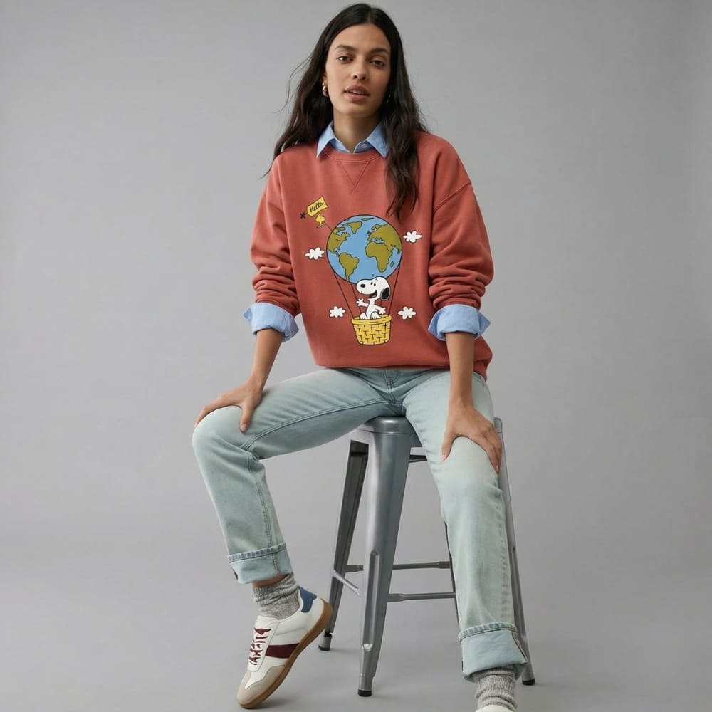 Person wearing a red sweater with a graphic design, sitting on a stool against a gray background